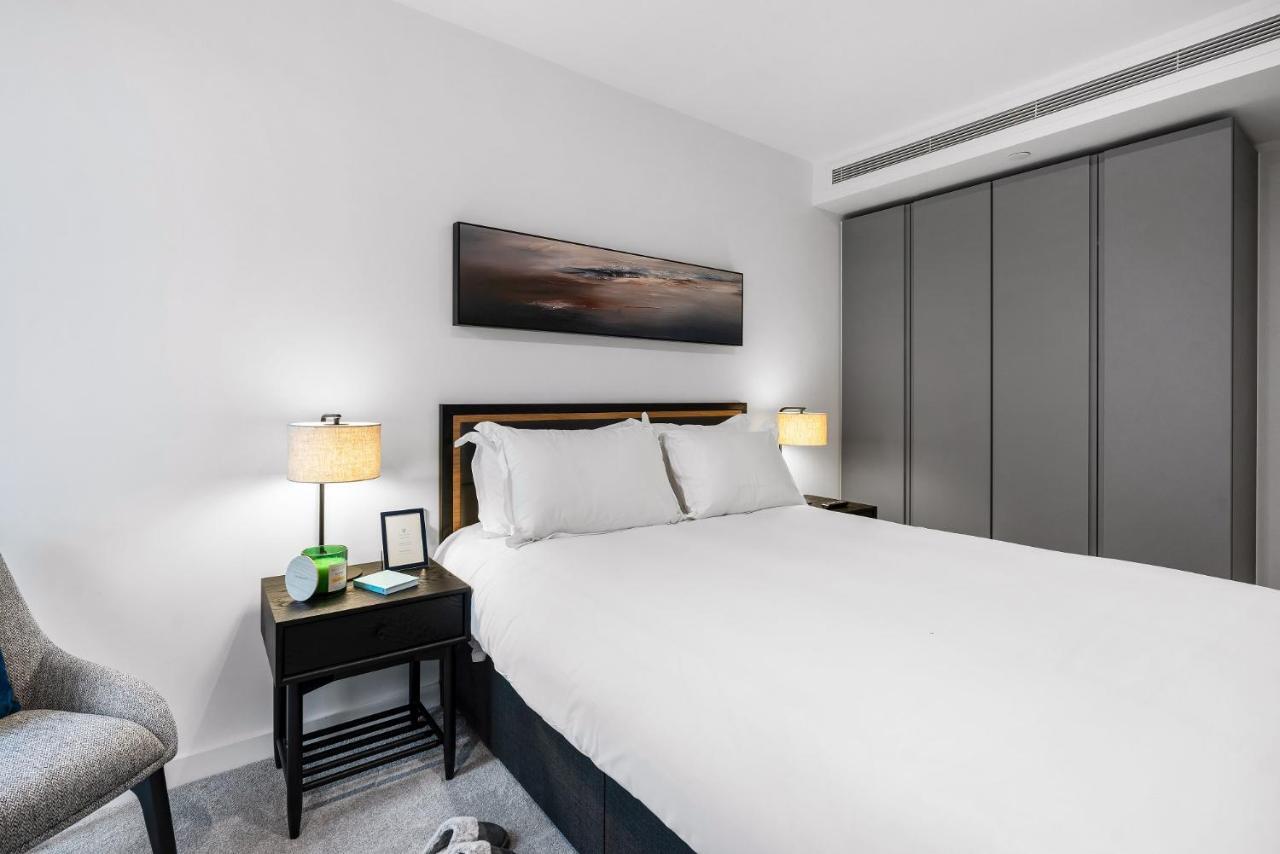 מנצ'סטר Citysuites 2 Aparthotel מראה חיצוני תמונה The photo shows a modern bedroom with a neatly made bed featuring white linens and pillows. Flanking the bed are two bedside tables, each with a lamp providing soft lighting. There is a piece of artwork above the bed, which appears to depict a landsc