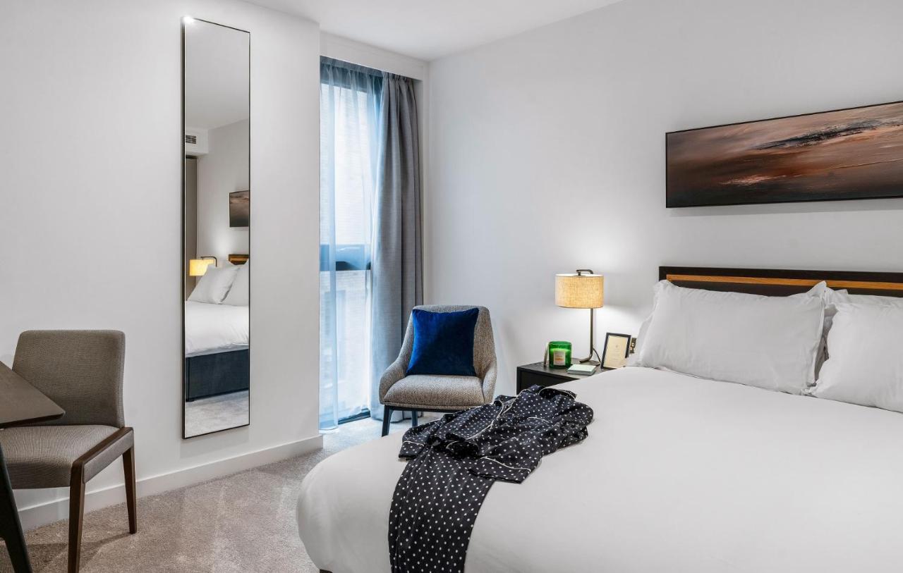 מנצ'סטר Citysuites 2 Aparthotel מראה חיצוני תמונה The photo shows a modern hotel room. It features a neatly made bed with white linens and a dark-colored throw draped over it. There is a small bedside table with a lamp next to the bed. A comfortable chair in a light color is positioned near the wind