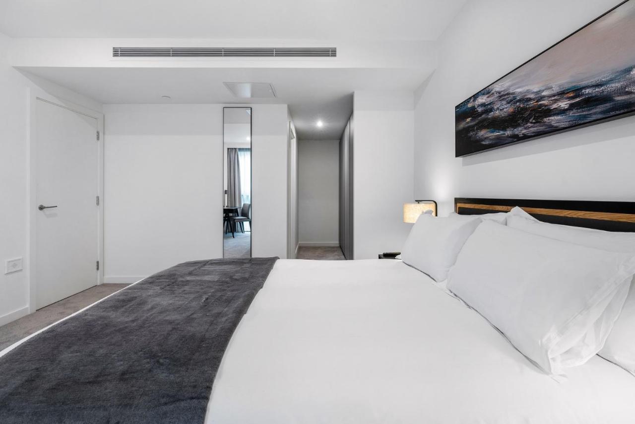 מנצ'סטר Citysuites 2 Aparthotel מראה חיצוני תמונה The photo shows a modern bedroom with a minimalistic design. In the foreground, there is a neatly made bed with white linens and a dark gray throw blanket. To the side, there is a bedside lamp and a piece of abstract artwork on the wall above the bed