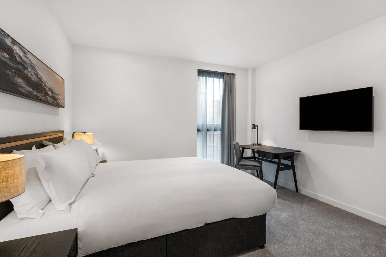 מנצ'סטר Citysuites 2 Aparthotel מראה חיצוני תמונה The photo shows a modern hotel room featuring a large bed with white linens and a dark headboard. There are two bedside lamps on either side of the bed. A desk with a chair is placed against one wall, and a flat-screen TV is mounted on another wall. 