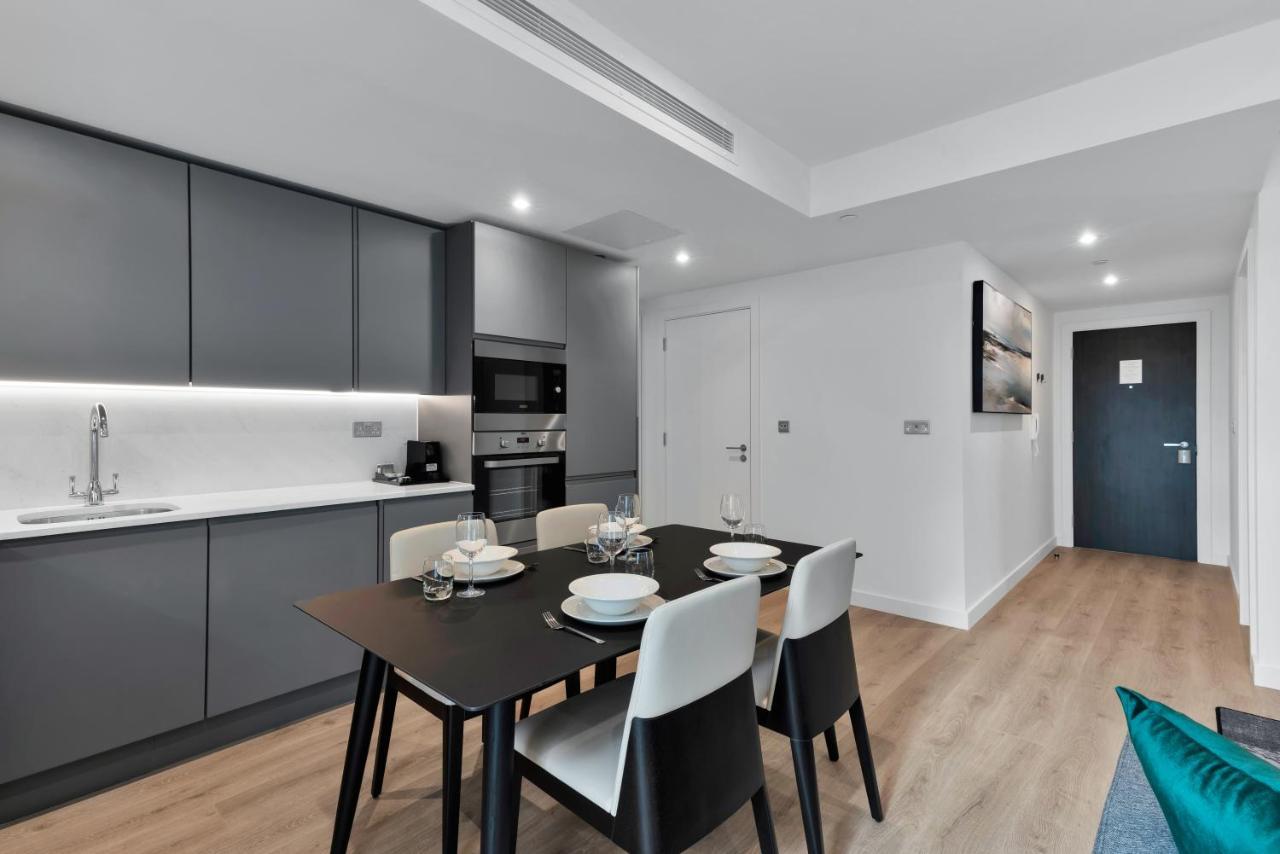 מנצ'סטר Citysuites 2 Aparthotel מראה חיצוני תמונה The image shows a modern kitchen and dining area. The kitchen features sleek gray cabinets with a white countertop, and it is equipped with appliances such as a microwave. There’s a dining table set for four, with white plates and glasses ready. The 