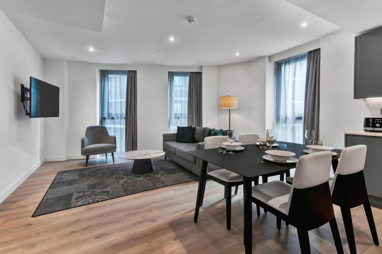 מנצ'סטר Citysuites 2 Aparthotel מראה חיצוני תמונה The photo shows a modern living space that includes a living area and dining area. 

- **Living Area**: There's a gray sofa with a coffee table in front of it, along with a single armchair. A large flat-screen TV is mounted on the wall. The space is 