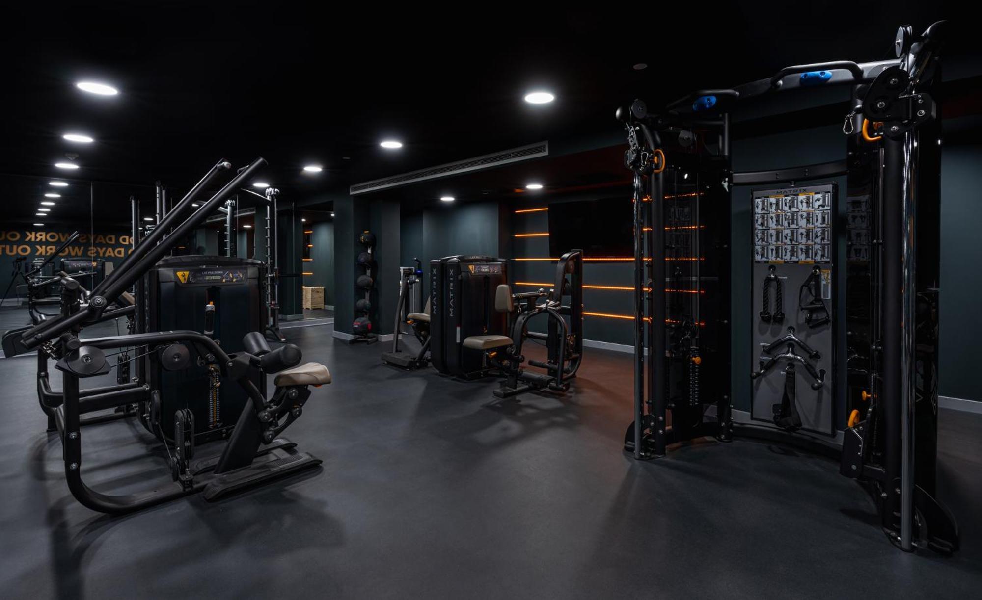 מנצ'סטר Citysuites 2 Aparthotel מראה חיצוני תמונה The photo shows a modern gym or fitness area with various workout machines. The space has a dark color scheme, featuring black walls and flooring. There are multiple pieces of exercise equipment, including stations for strength training, possibly tar
