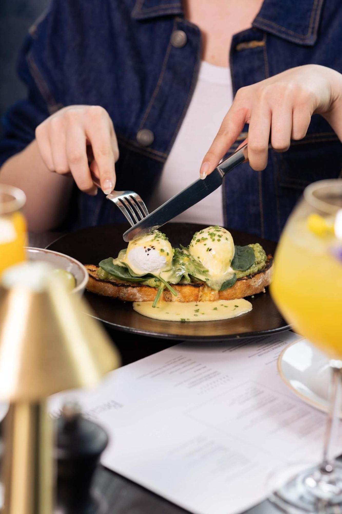 מנצ'סטר Citysuites 2 Aparthotel מראה חיצוני תמונה The photo shows a person preparing to eat a dish of eggs Benedict. They are holding a knife and fork, ready to cut into the meal, which features poached eggs on top of a slice of toast, accompanied by spinach and a creamy hollandaise sauce drizzled o